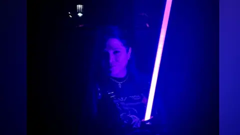 Jessica Monger Jessica Monger in subdue light in a Star War s outfit holding a light sabre