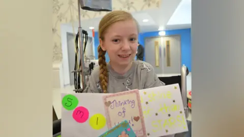 Katie Callaghan Katie Callaghan as a 13-year-old holding some of the cards she made for others while sat in a hospital.