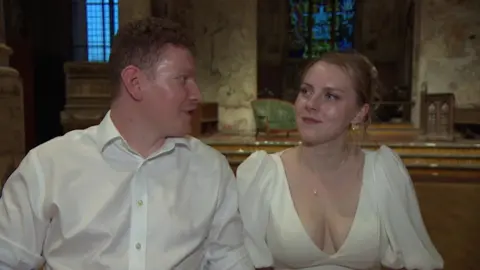 Ryan and Freya Sedgman are looking at each other inside a church.