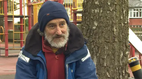 A councillor, sitting on a bench in a children's playground.