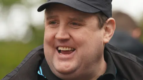 Peter Kay smiling in a baseball cap in 2022