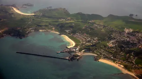 BBC A view of Alderney from the air. A small island with yellow sandy beaches.