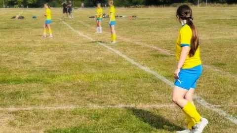 Young Women's Football Academy Several young girls in yellow football tops and blue shorts on a grassy football pitch.