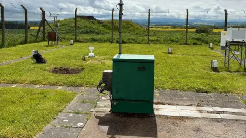 Met Office A weather station with a large green box in the middle of it and fencing round the outside