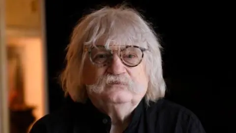 Karl Jenkins looking at the camera. He is wearing dark glasses and a dark shirt. 