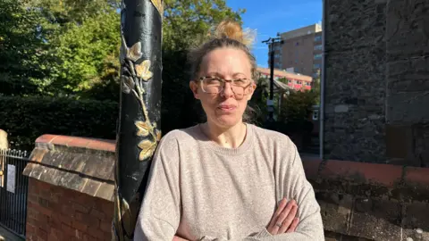 Ms McKie leaning against a black lamp post with her arms crossed