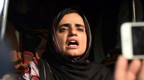 EPA Mahrang Baloch  in a head scarf with her mouth open mid-speech
