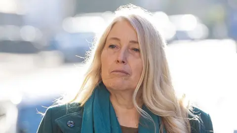 PA Media Sacha Dench is outside. It is a sunny day and sunlight is reflected on objects behind her. Dench has long blonde hair and is wearing a green coat and green scarf.