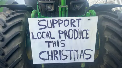 A white sign on a green tractor, which says 'support local produce this christmas' in black letters.