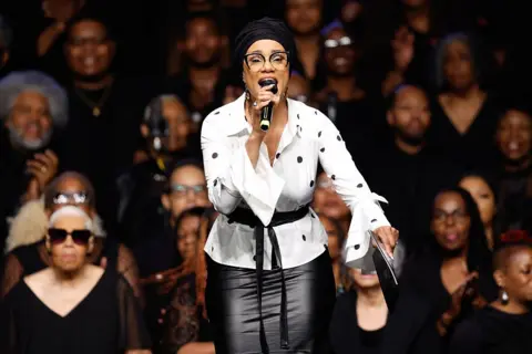 Getty Images US singer Opal Staples sings in front of the audience, wearing a black and white polk-a-dot blouse and a black leather skirt.