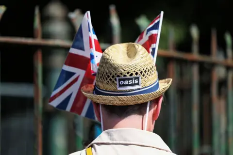 Rear view of a man wearing a straw sun hat branded with the black and white Oasis logo and union flags on either side of his hat