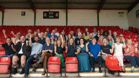 A group of people sitting in football stands cheering.