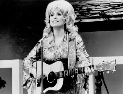 Michael Ochs Archives/Getty Images Black and white image of Dolly Parton on stage with a guitar
