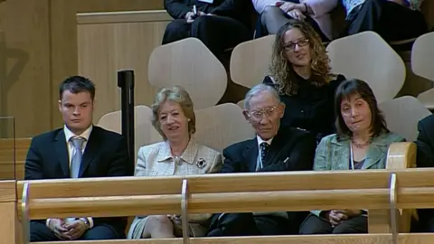 A group of four people watching events in the Scottish Parliament. Moira Salmond is second from left and Salmond's father is sitting to the right of her.