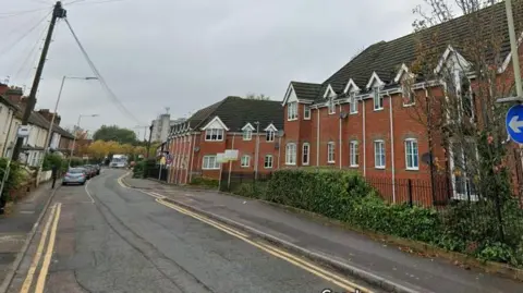 A screenshot from Google street view showing a residential road with houses on either side, and double yellow lines running next to the kerbs.
