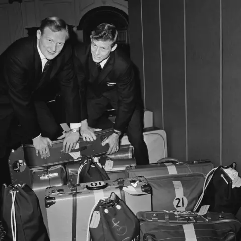 Getty Images Black and white image of Arthur Smith and another rugby player in suits with a set of suitcases as they embark on a British and Irish Lions tour