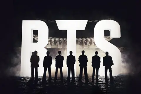 Netflix A promotional photo of BTS. The band are in silhouette, standing in front of a giant illuminated logo of their name