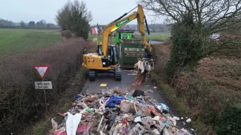 Contractors work to remove a pile of waste from Watery Lane, on the outskirts of Lichfield in Staffordshire.