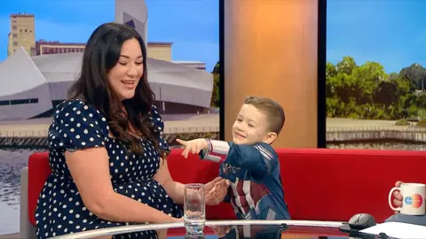 Isaac points at the camera while he and his mum are sat on the BBC Breakfast studio
