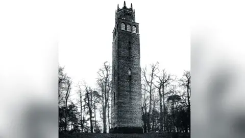 Getty Images A black and white picture of the tower, which has a small window about half way up and then three windows at the top. It is surrounded by trees.
