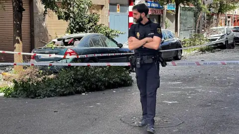 A policeman stands at a cordoned off street near damaged vehicles following an earthquake in Granada, southern Spain. Photo: 18 August 2026