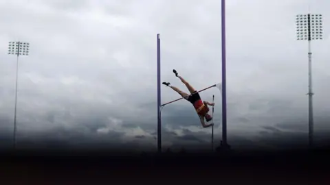 Getty Images A woman jumps over a pole. 