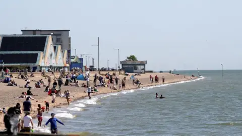 People sitting and playing on the beach in Southend in sunny weather. There are also people in the sea. 