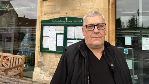 Phil Exton, Mayor of Malmesbury, pictured in front of a Town Council sign. 