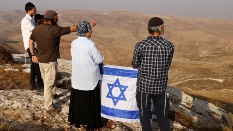 A group of Israelis with an Israeli flag look out across hilltops in the occupied West Bank (November 2022)