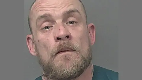 Police mugshot of Philip Gonsalves. He has a light-coloured beard and short hair. He is looking at the camera with his head tilted to the right.