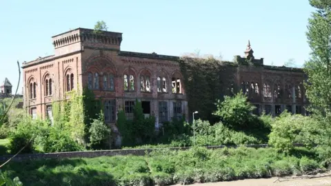 Nick Ward A dilapidated mill building on the banks of the River Nith in Dumfries with plants growing all around it and over it
