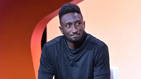 Getty Images Marques Brownlee shown sitting on stage during an interview at a tech conference against a colourful background.