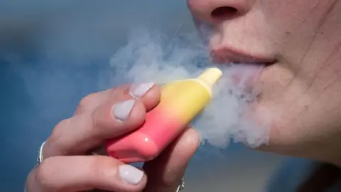 A close up of a person smoking from a pink and yellow disposable vape