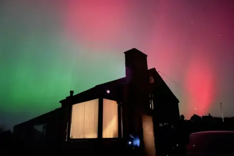 Emily Morgan Pink and green Northern Lights over a silhouetted bungalow