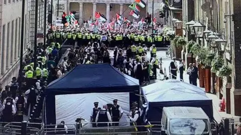 Metropolitan Police Police and arrested protesters gather near a holding area while they wait to be processed