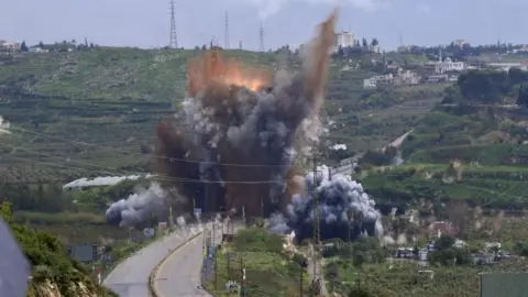 EPA Smoke and fire after an attack on a bridge in southern Lebanon in the middle of a road with green fields on both sides and buildings in the distance including a mosque