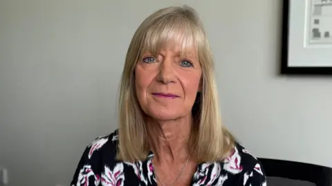 Andrea Nightingale. She is wearing a black floral top, and has blonde hair and a fringe.