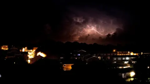 Brendan Lightning in a dark purplish sky over a neighbourhood.
