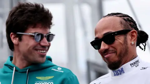 Aston Martin driver Lance Stroll and Ferrari driver Lewis Hamilton smiling while in conversation at the 2026 Australian Grand Prix. Both men are wearing sunglasses