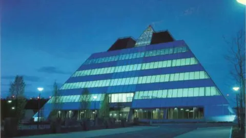 Stockport Pyramid at night shortly after its completion, with lights on at night. The imposing front face can be seen leading up to the tip. 