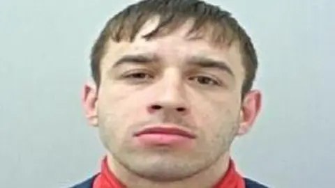 Police custody image of Terrence Kenny with brown hair and eyes wearing a red polo neck top and black jacket.