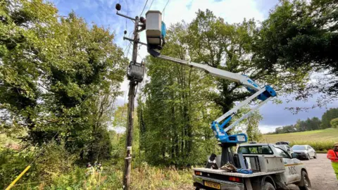 An engineer in a cherry picker working to fix on a power line.