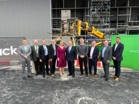 BBC/Richard Edwards A group of people, including North Yorkshire mayor David Skaith stand in front of the construction of the new Schneider plant in Scarborough