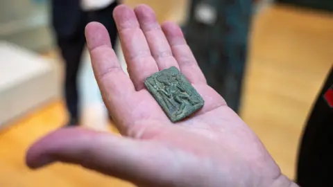 Kent County Council A hand holding a small metal stamp with a man on it