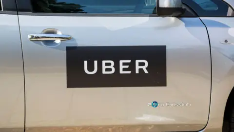 A silver car with an Uber symbol on its driver's door and a zero emissions badge in the bottom right-hand corner of the door.