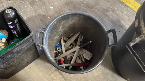 A birds-eye view of a black bucket with knives and scissors in it.