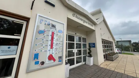 BBC A school building with a main entrance and 'd'Auvergne School' sign above, granite square floor, grey skies behind 