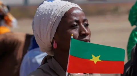 AFP A woman wearing headscarf and pink earrings waves the flag of Burkina Faso