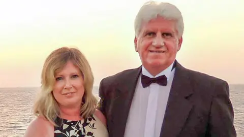 Pacemaker Susan Baird and Gary Baird in formal dress in front of a body of water with sunset in background