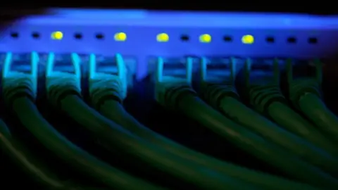 The back of a server rack showing seven cables plugged into the rack which is blue with yellow/green lights above each cable.